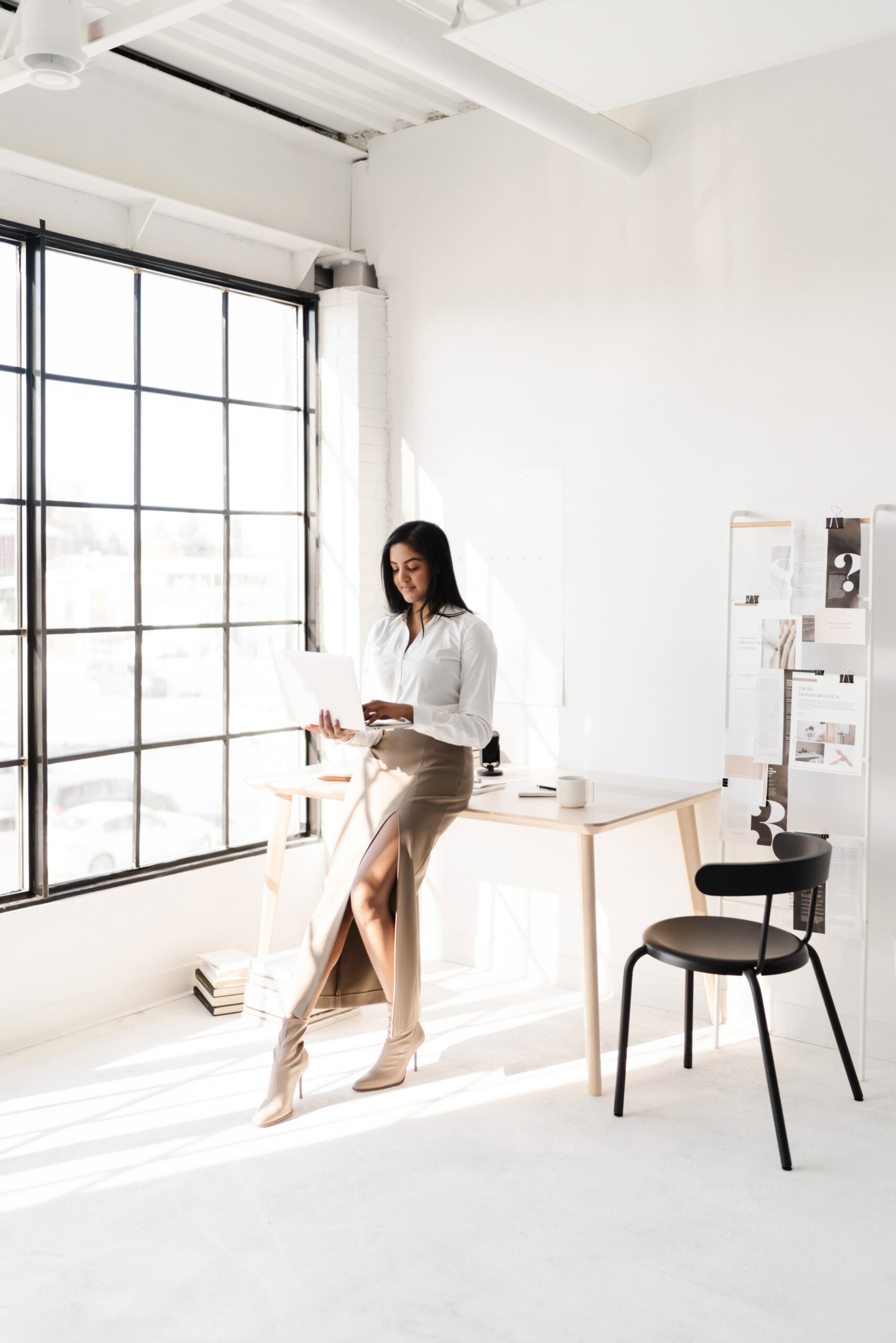 Woman of color business owner looking thoughtfully at her laptop, reviewing her website and brand presence in a clean, professional workspace.
