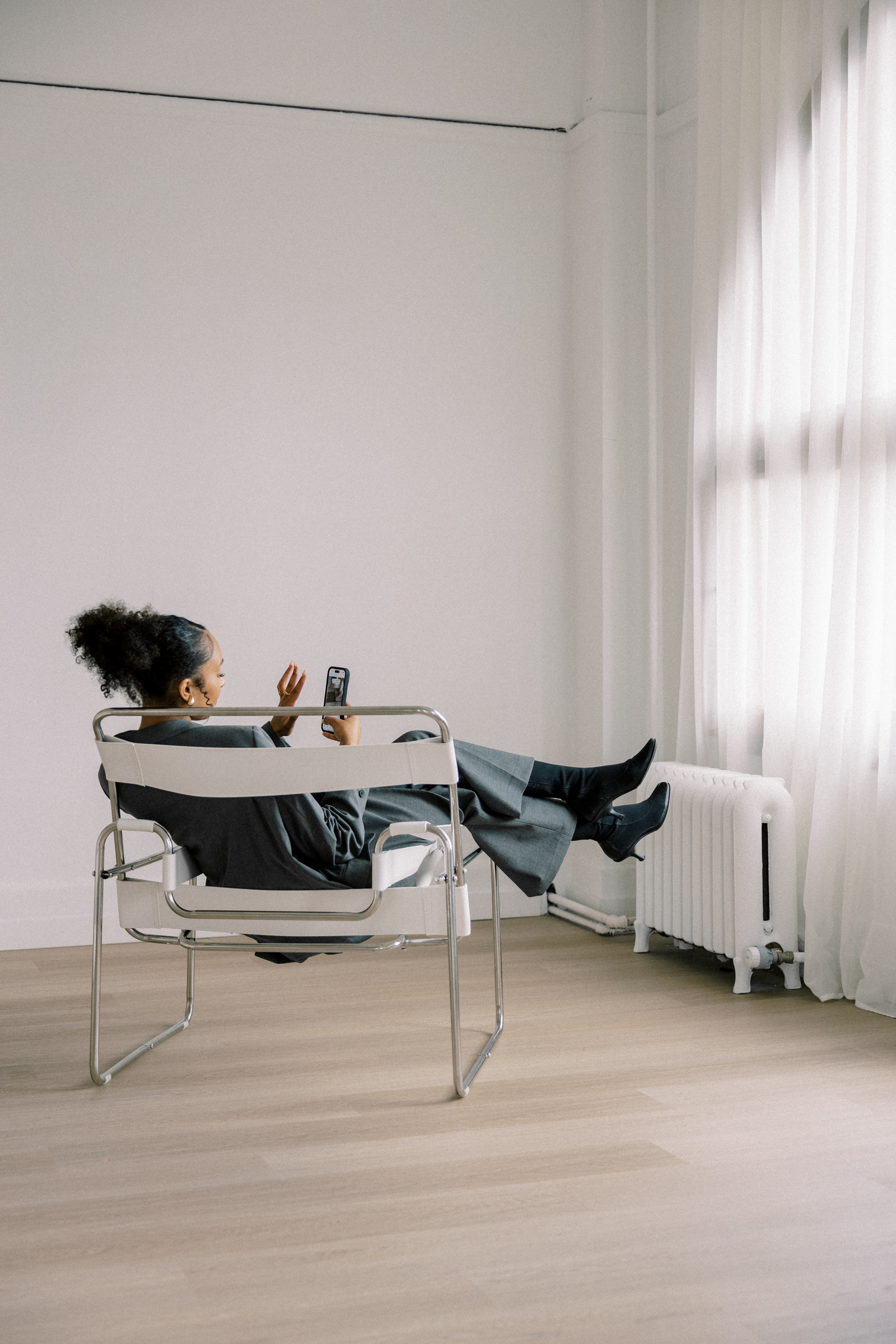 Woman of color business owner sitting confidently at a clean desk, relaxed, looking away from screen, natural light, elevated workspace.